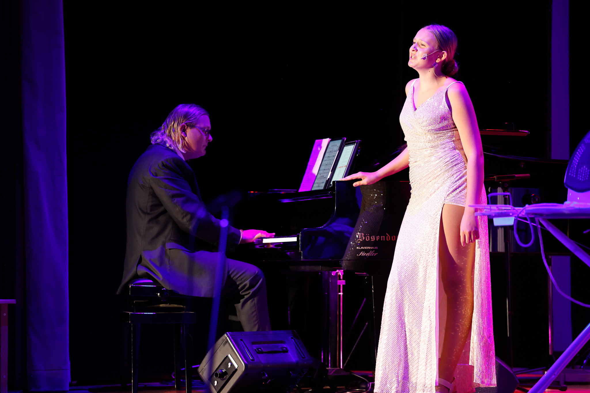 Sängerin im weißen Glitzerkleid singt am Flügel zur Begleitung des Pianisten
