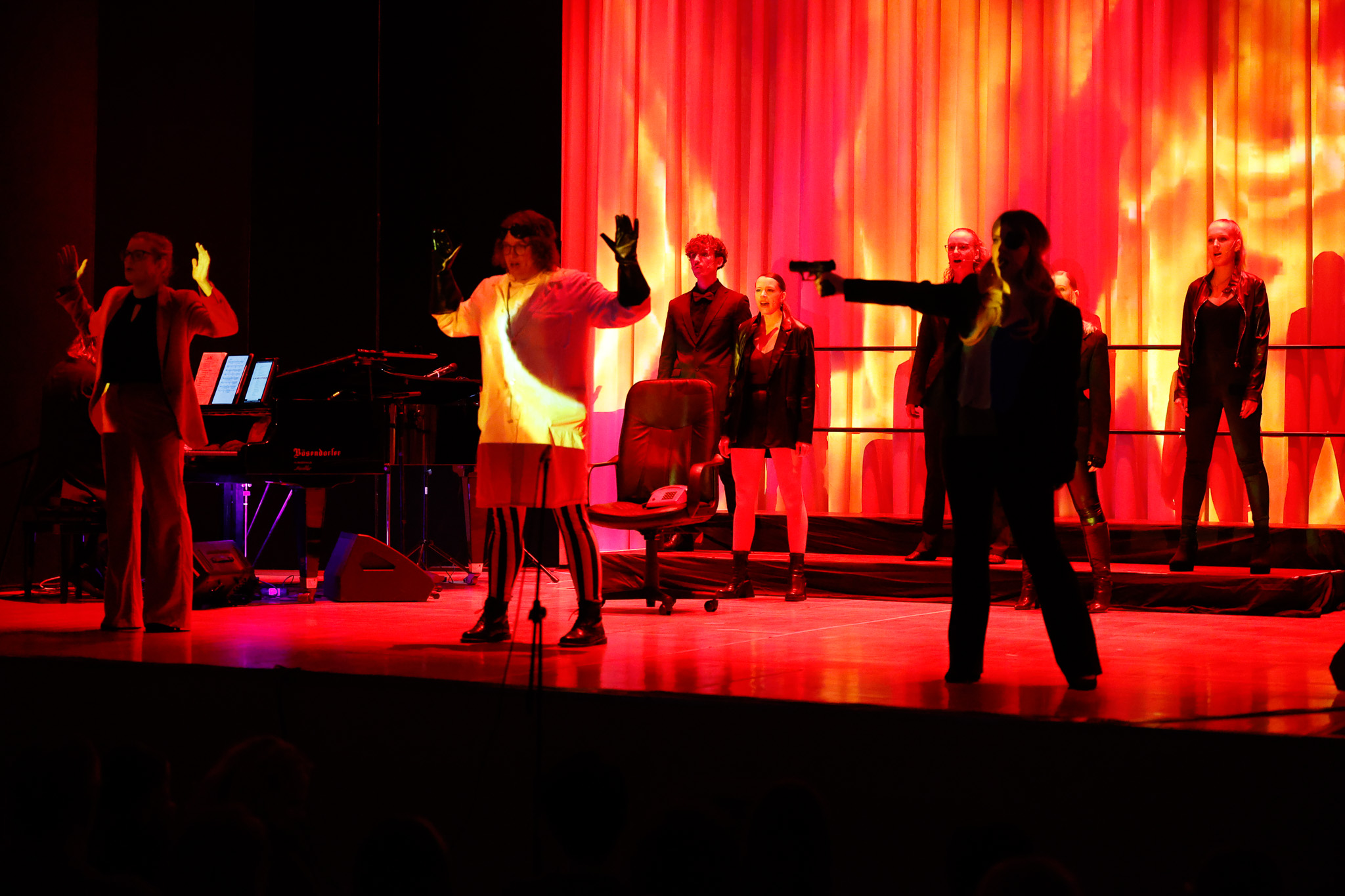 Ensemble in einer dramatisch rot beleuchteten Konfrontation auf der Bühne